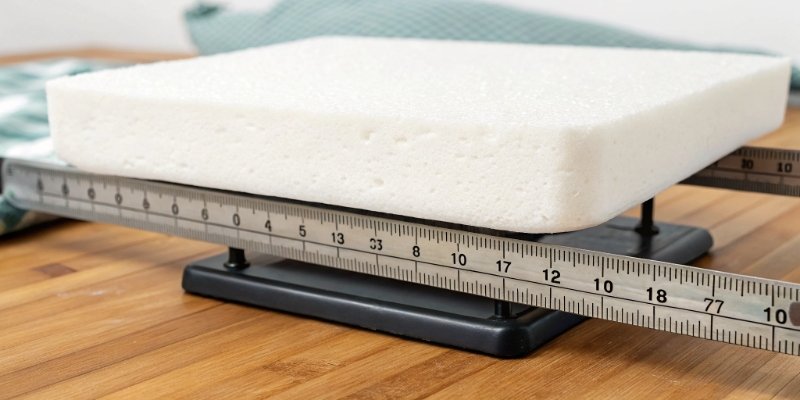 A diagram showing a foam cushion on a scale (Weight) and a ruler measuring its dimensions (Volume), with an arrow pointing to the formula Density = Weight / Volume.