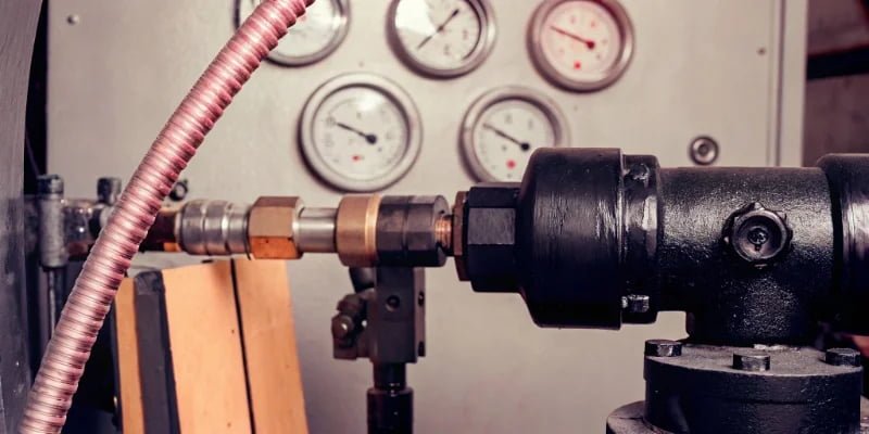 A high-pressure PU foaming machine mixing head with pressure gauges in the background